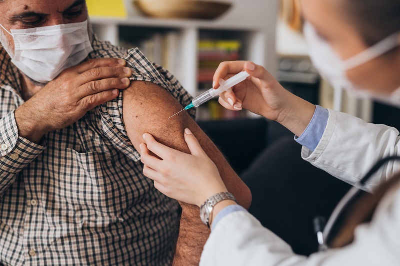 man wearing mask gets a vaccine in his arm at home
