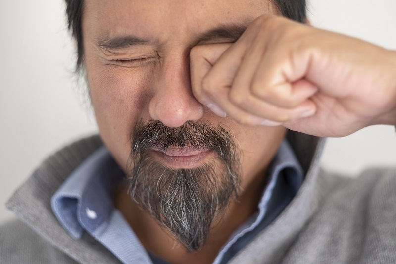 Close up shot of man with an eye floater rubbing his eye due to an eye floater.